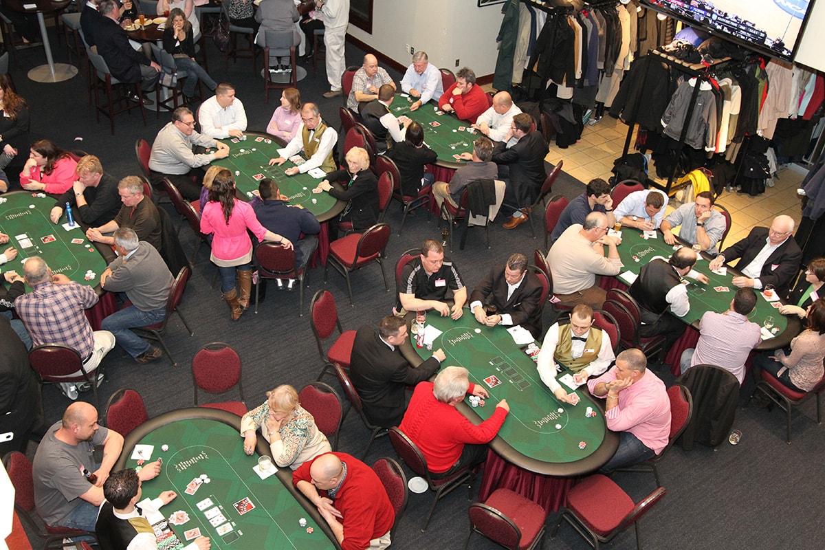 Aerial view of a packed Boston casino party with multiple poker tables full of guests and professional dealers