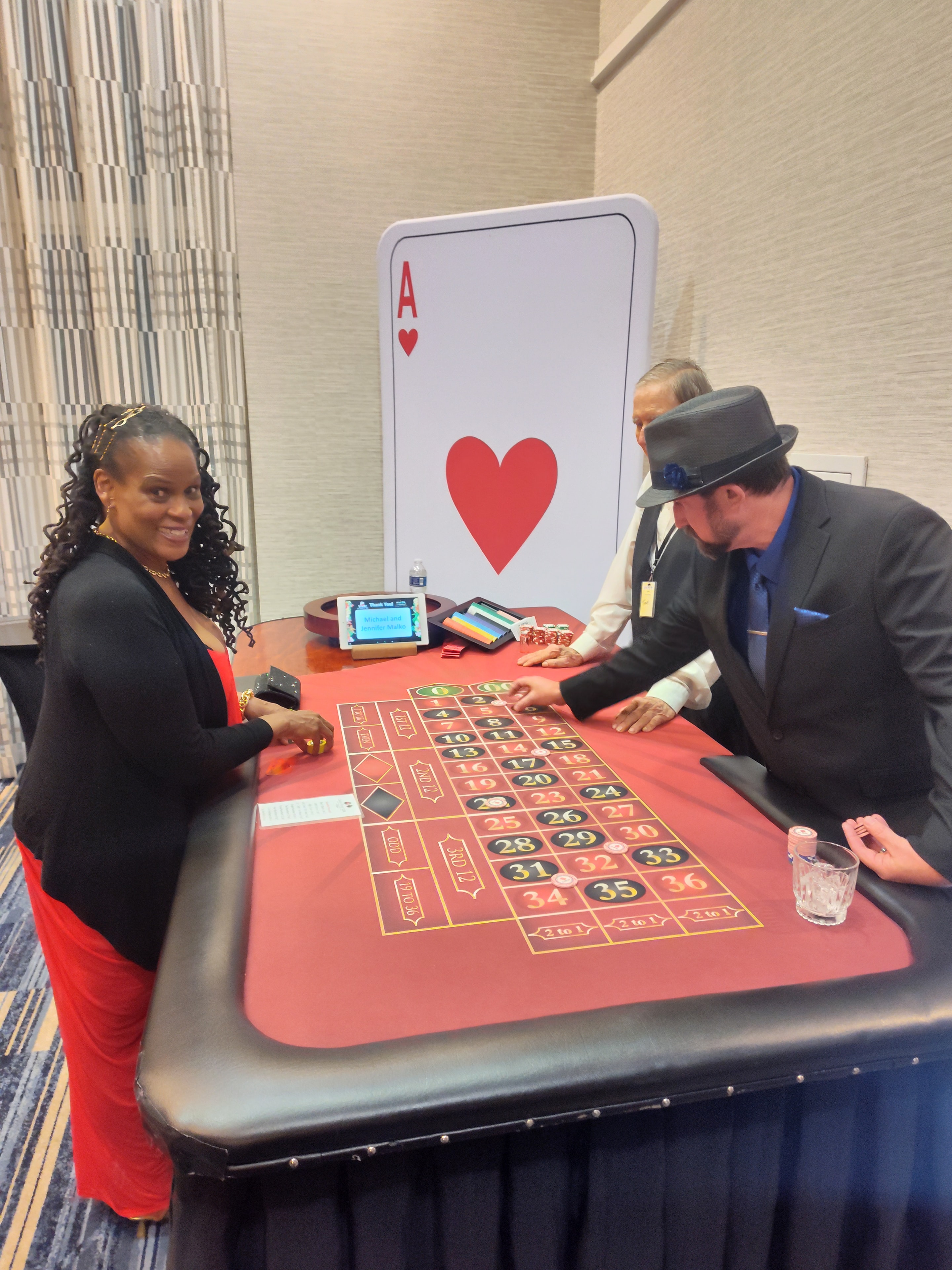 Dealer and guest at a Casino Party USA roulette table with giant playing card backdrop in Colorado Springs