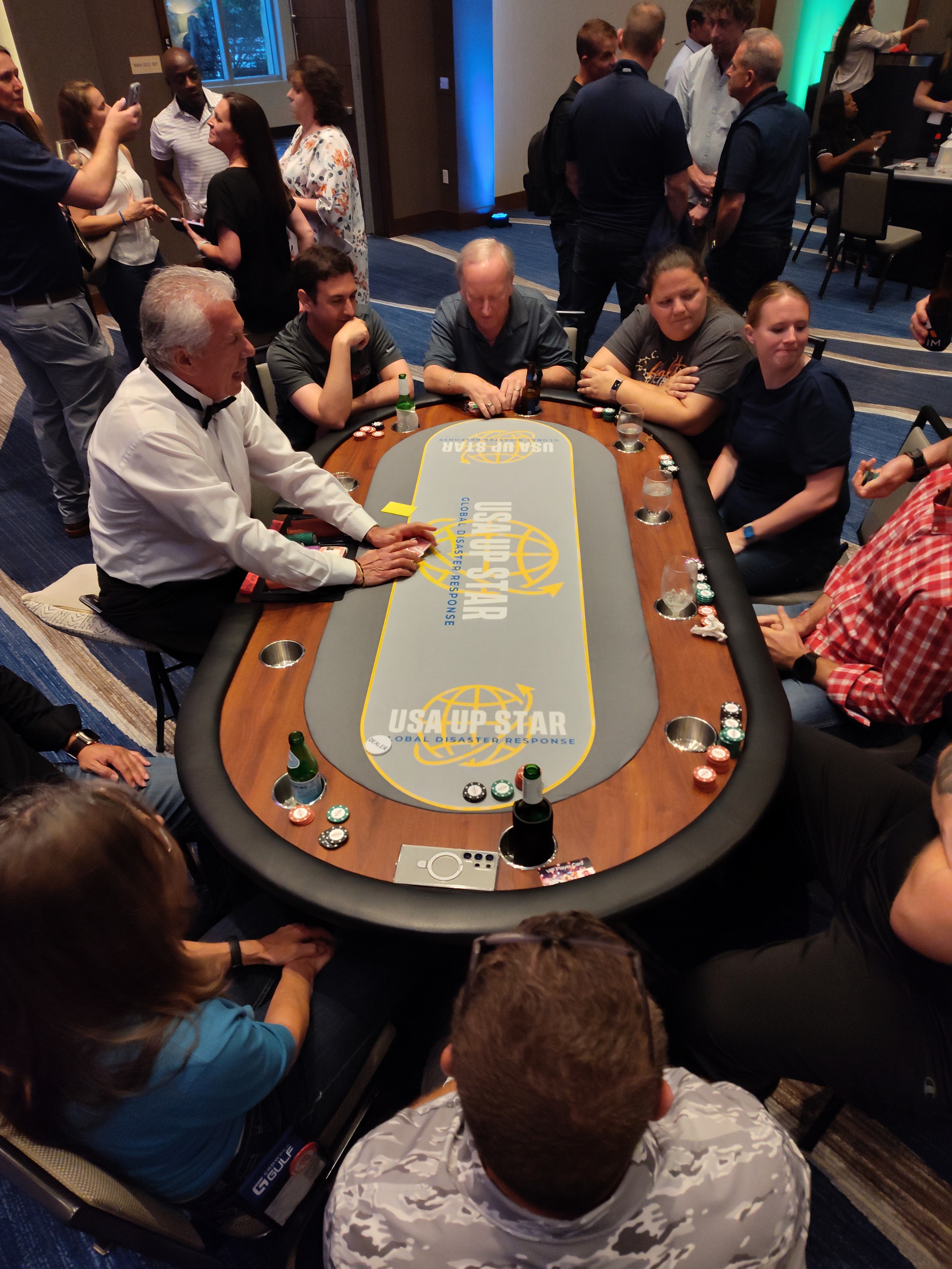 Overhead view of custom branded poker table felt with USA UP STAR corporate logo surrounded by casino party guests