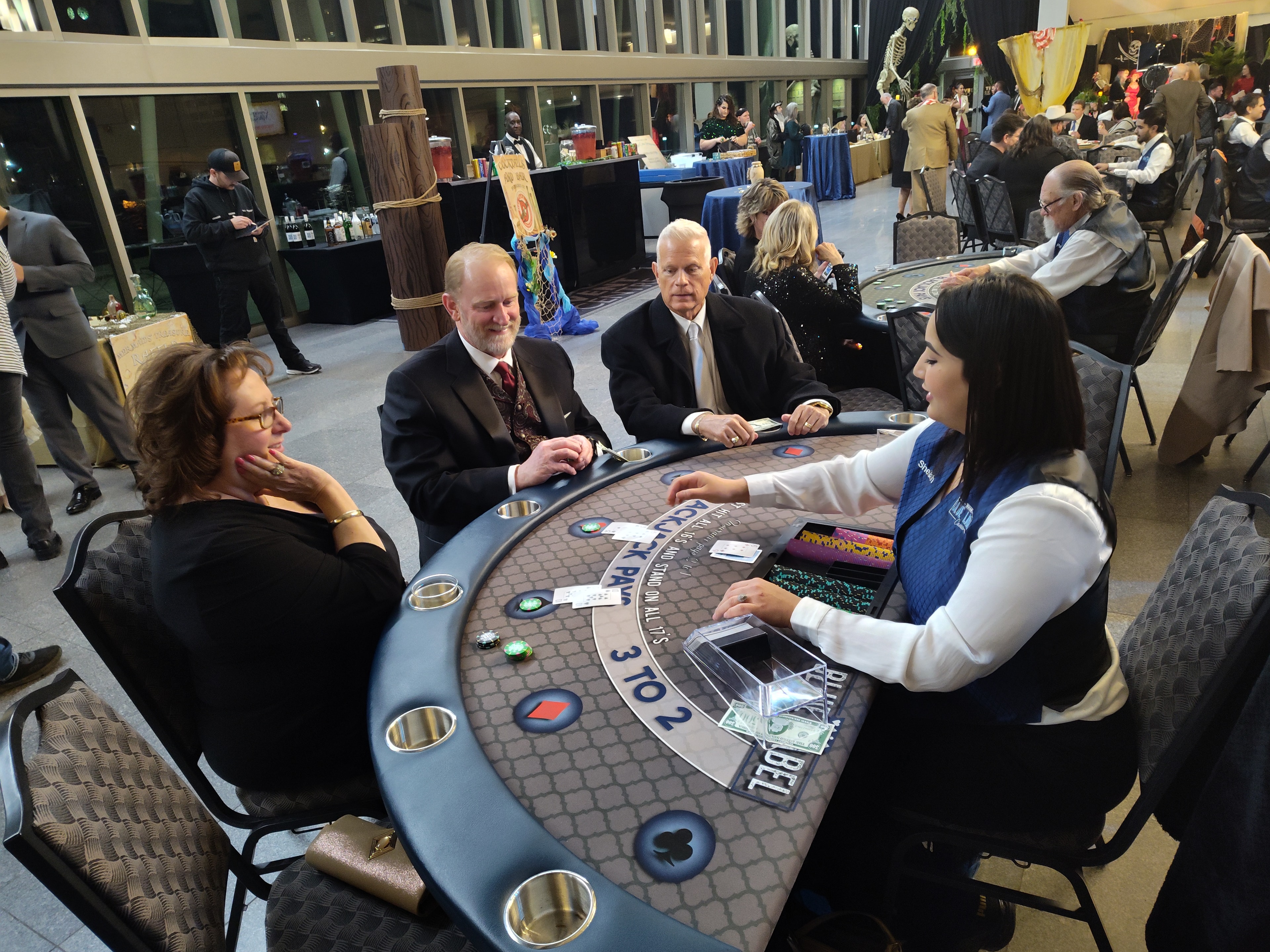 Guests in formal attire playing blackjack at a Blue Label Casinos Houston event with Halloween skeleton decor