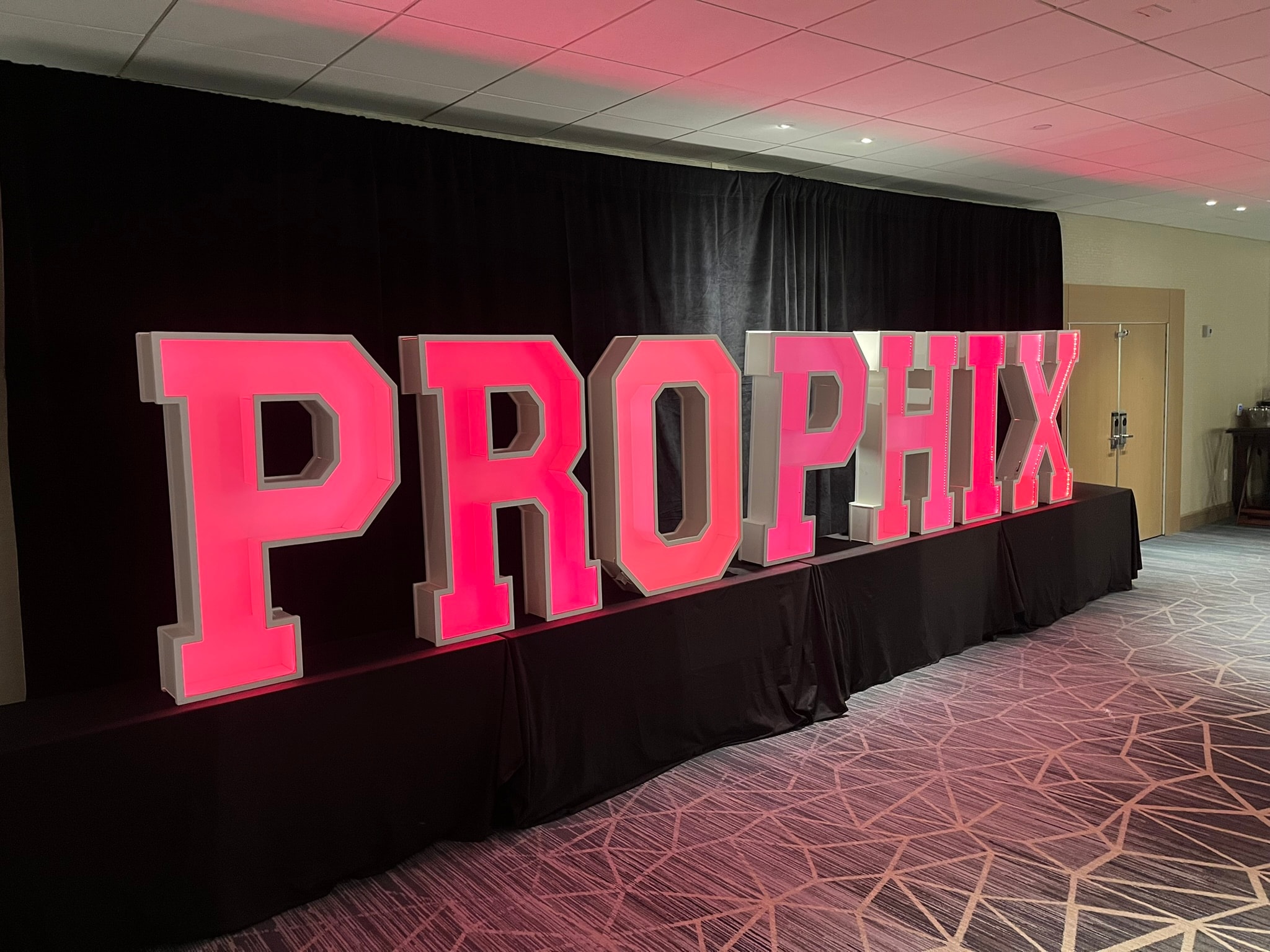 Illuminated marquee letters spelling PROPHIX in neon pink at event venue