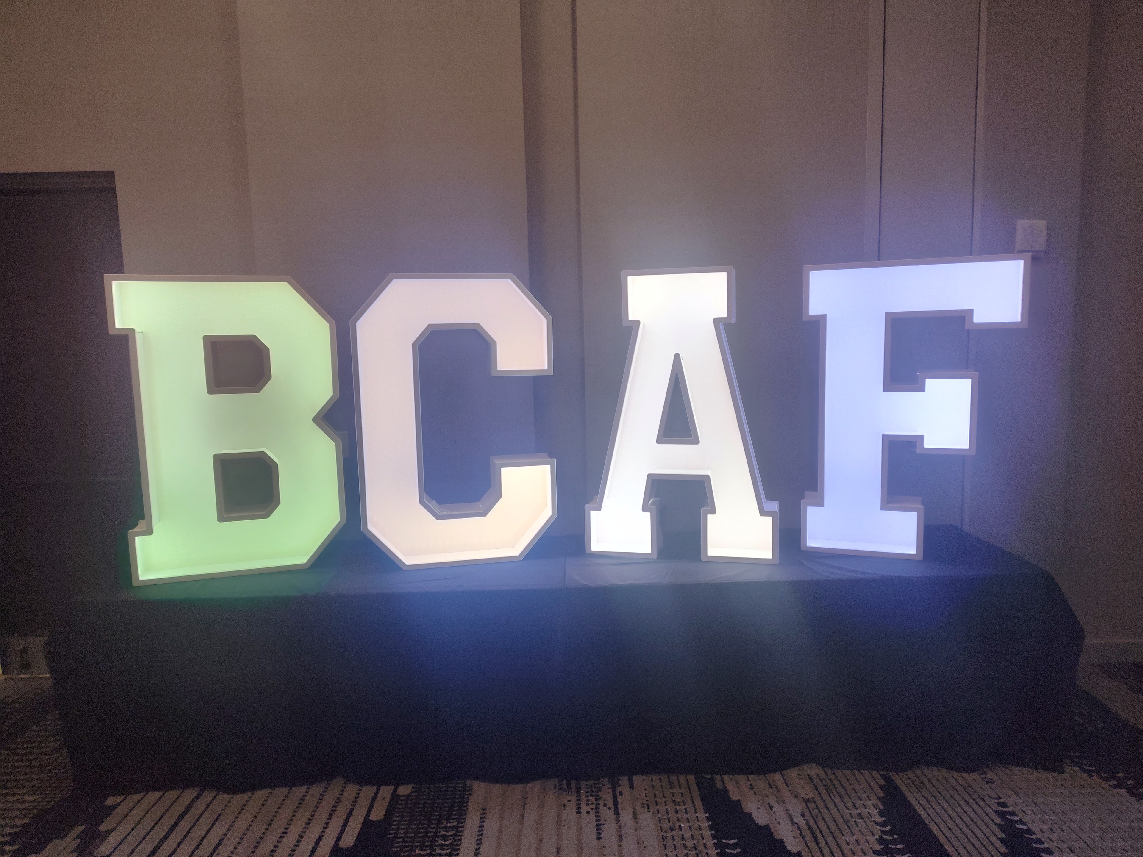 Illuminated marquee letters BCAF in green and white on display table at event