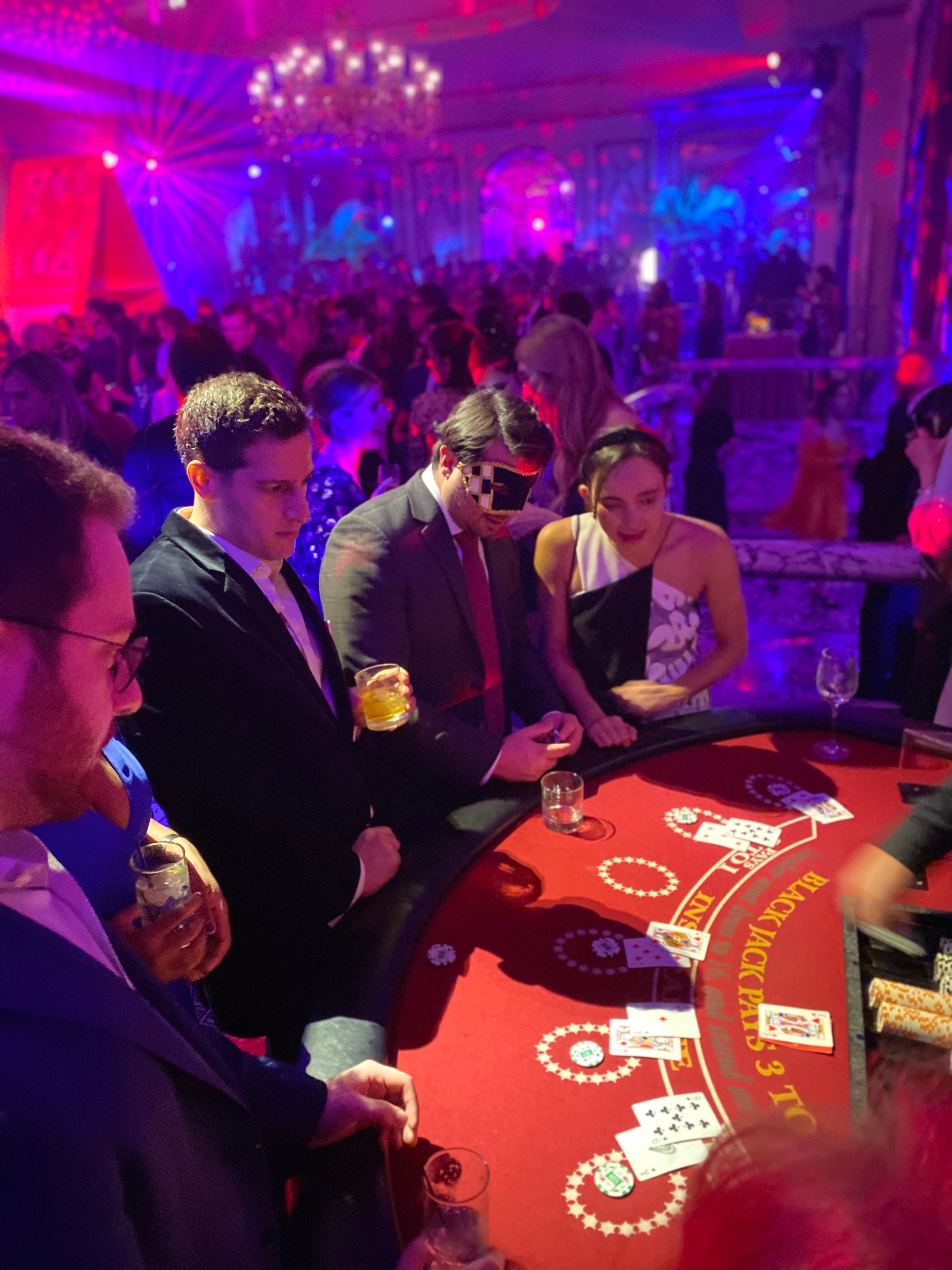 Guests in formal attire playing blackjack under vibrant purple and blue lighting at a New Jersey Purim Ball casino party