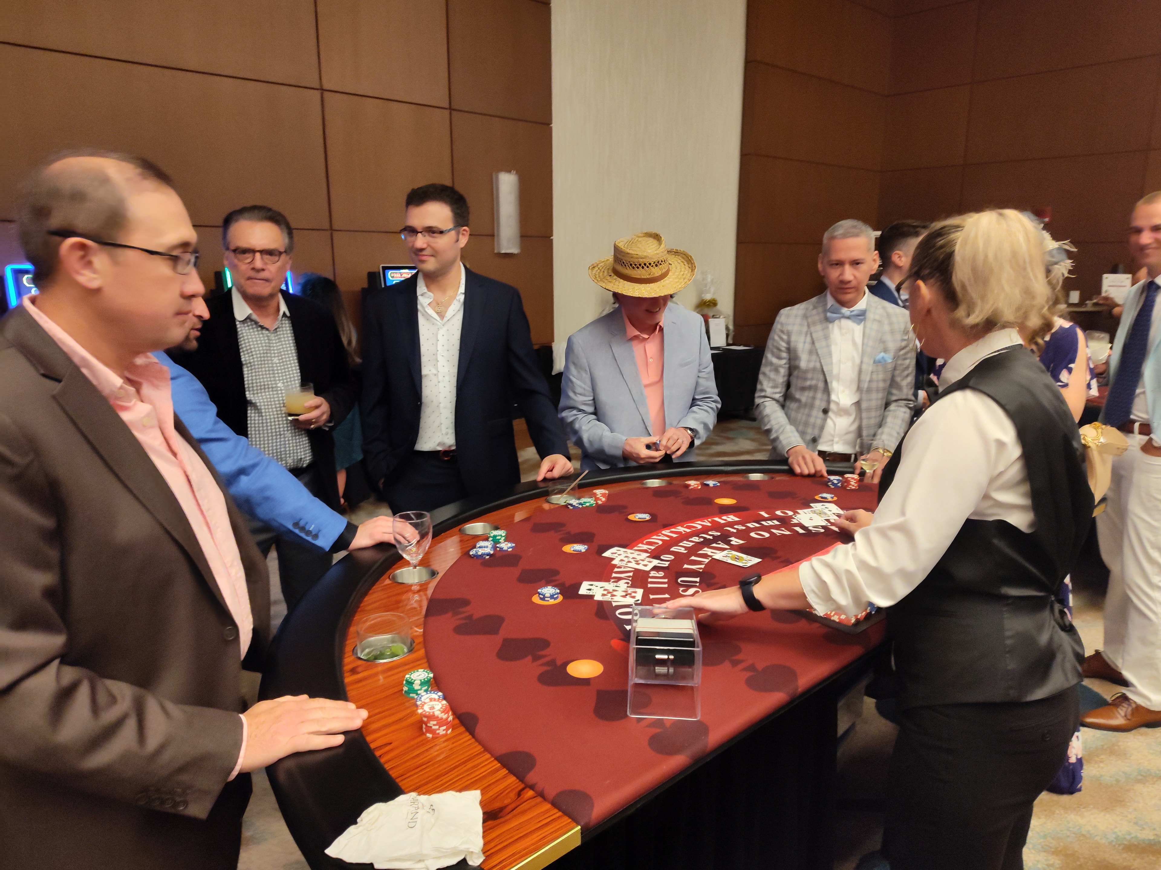Guests in straw hats crowded around a Casino Party USA blackjack table at an Orlando event