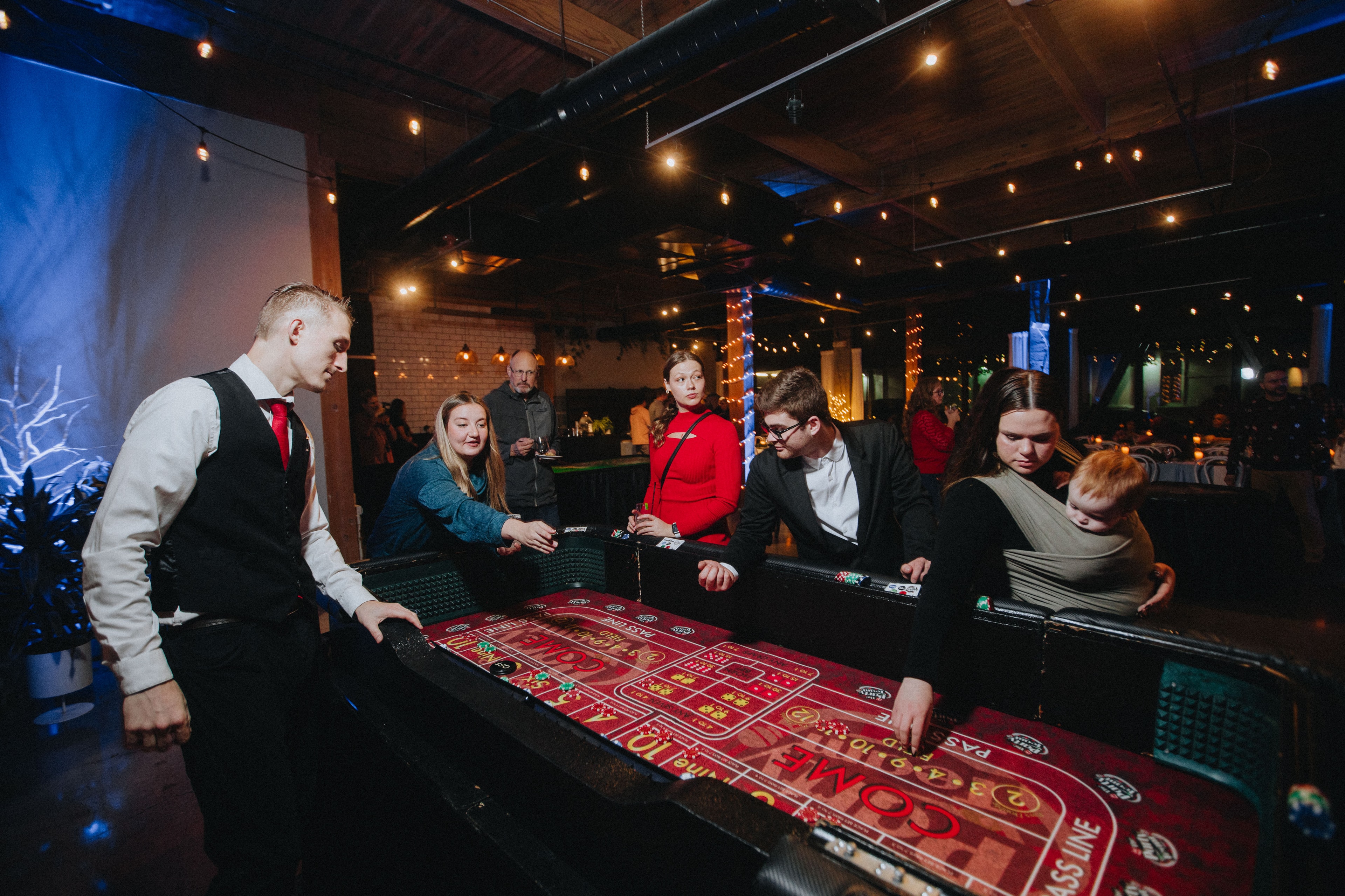 Dealer running a craps table at a Portland Oregon holiday casino party with string lights