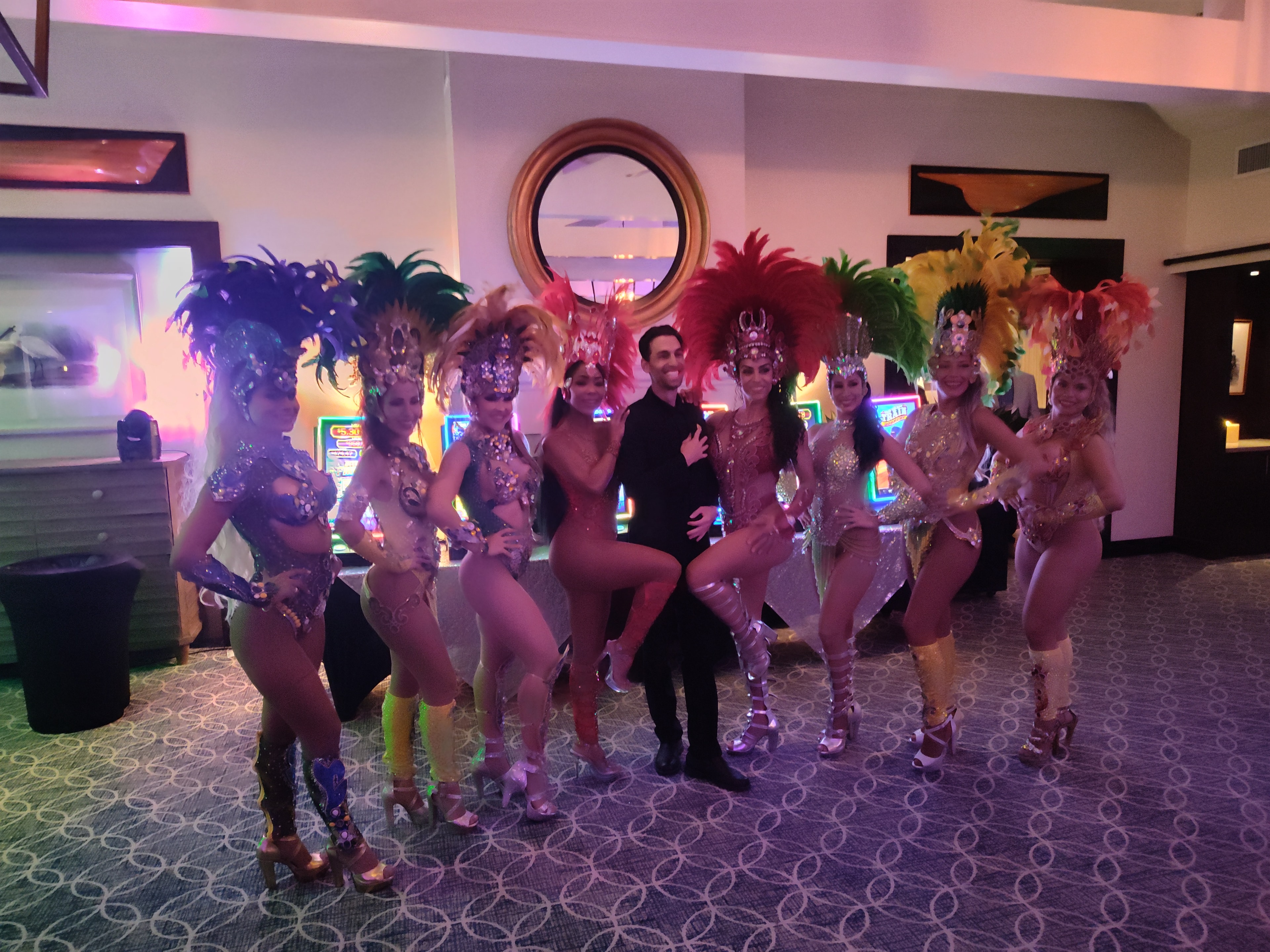 Showgirls in elaborate feathered costumes posing with guests at a Tampa Casino Party USA event