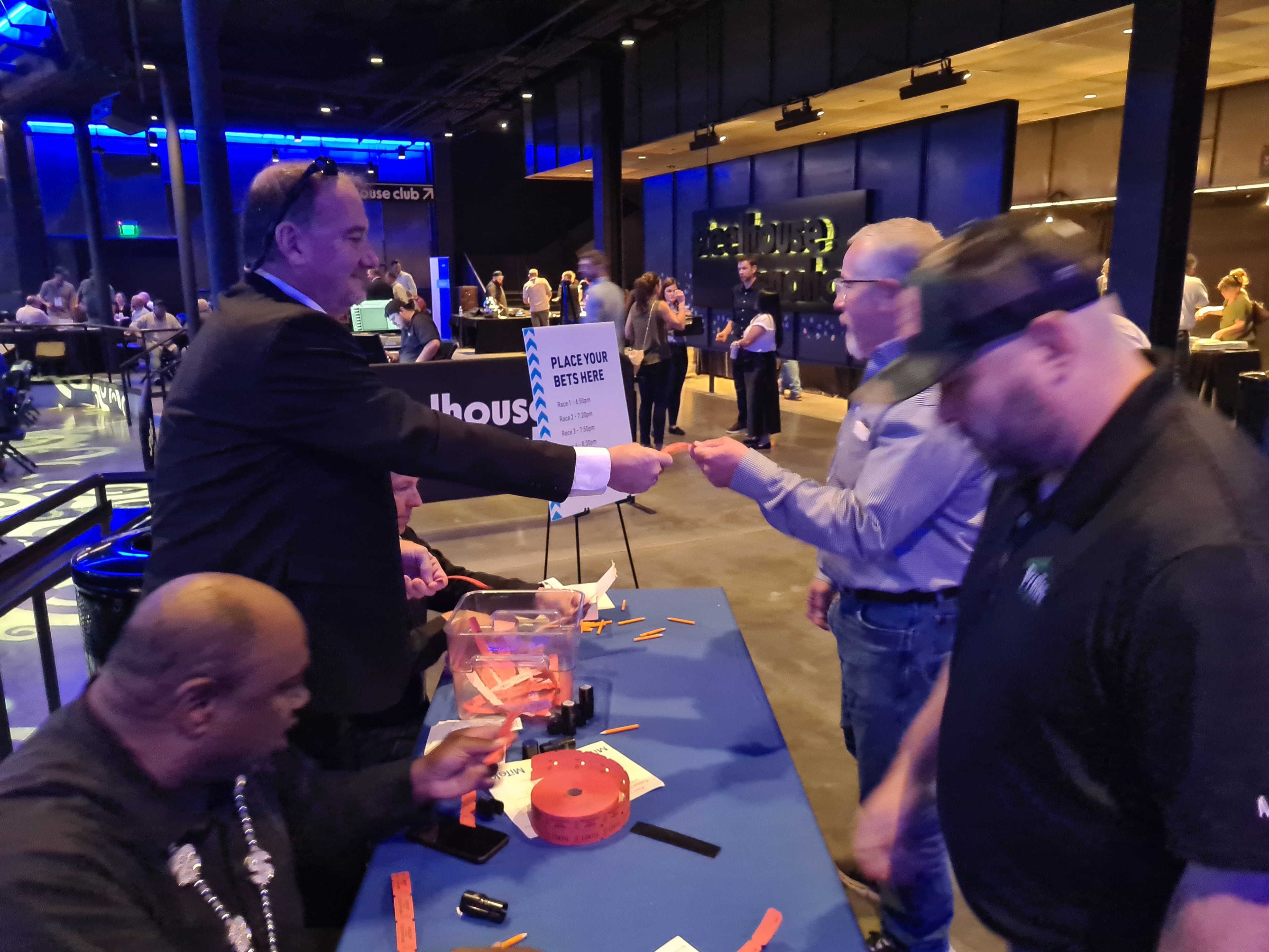 Casino Party USA staff handing out betting slips to guests at a Place Your Bets Here table at a corporate horse racing event